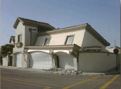 Damaged white two-story house with collapsed garage and cracked front facade after an earthquake