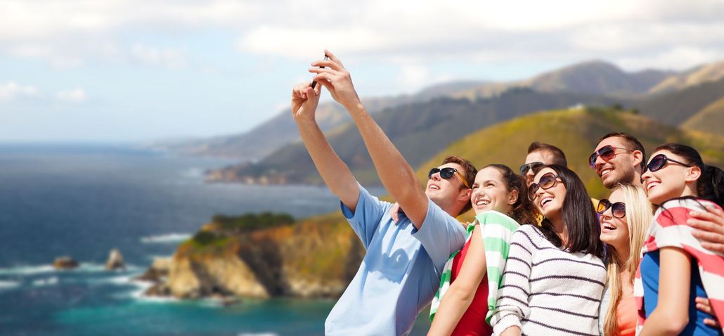 Group of people taking a selfie outdoors with a scenic ocean and mountain backdrop. Group of people taking a selfie outdoors with a scenic ocean and mountain backdrop.
