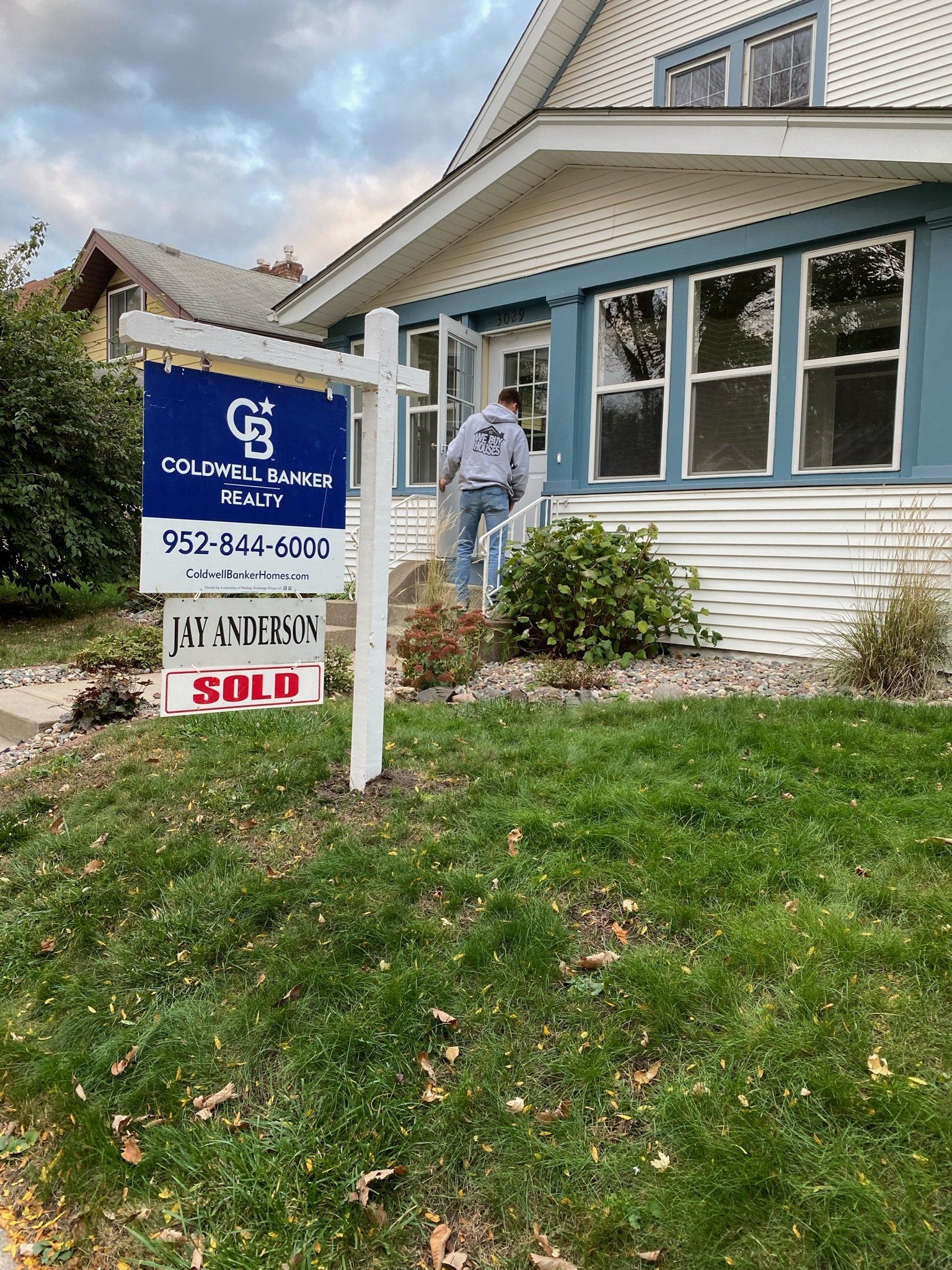 A man is standing in front of a house with a for sale sign in front of it.