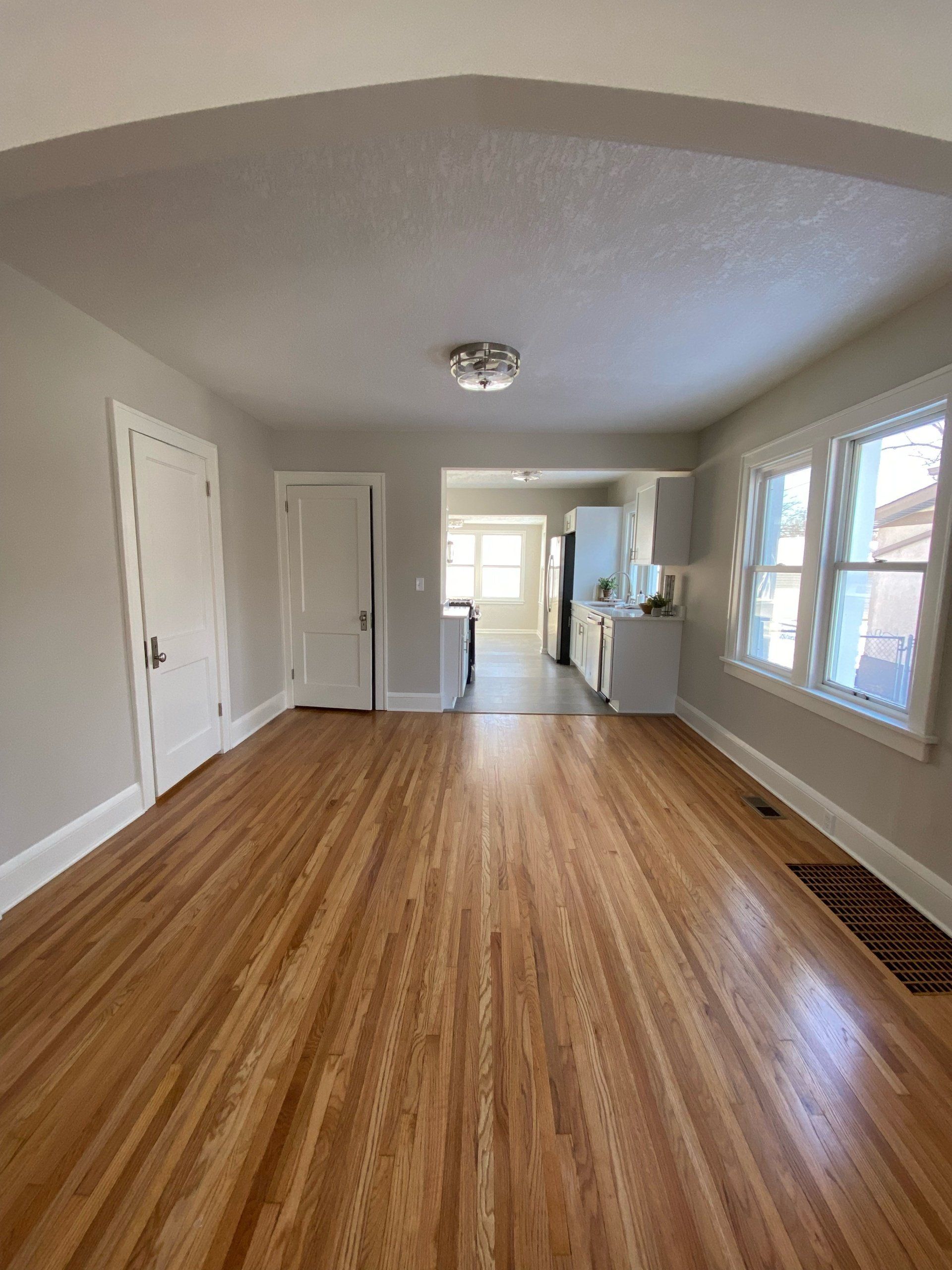 A living room with hardwood floors and a kitchen in the background.