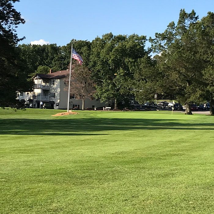 Sunny grassy field with a flagpole and an American flag beside a house and trees