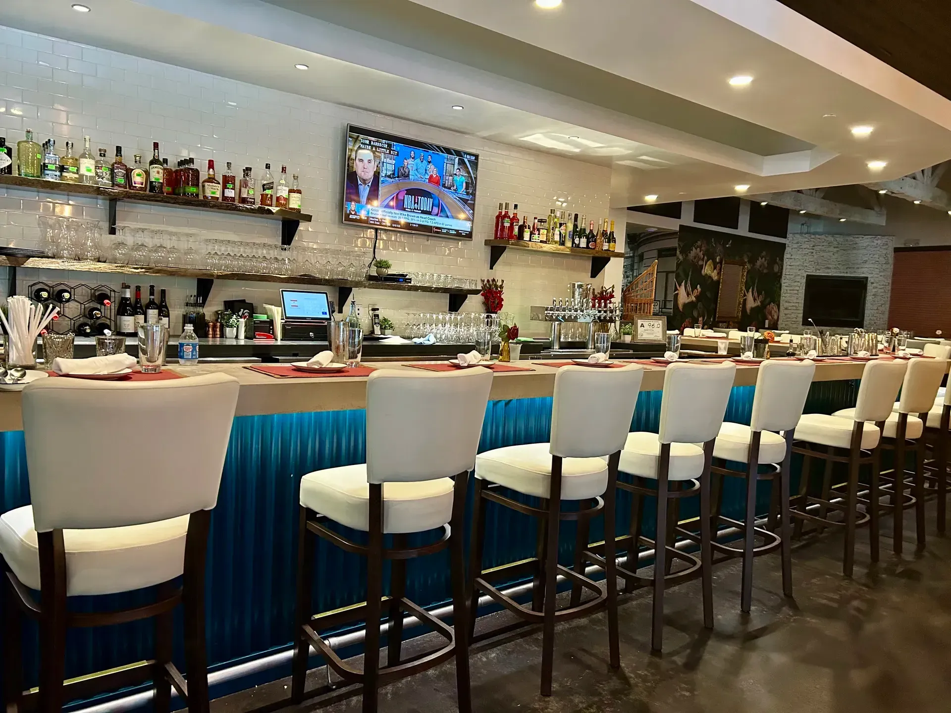 Bar with white stools, liquor bottles, a TV, and blue and wood accents.