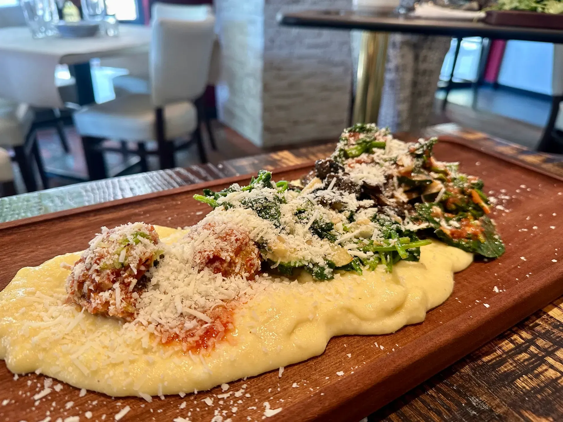 Polenta with meatballs and vegetables on a wooden board, sprinkled with Parmesan cheese.