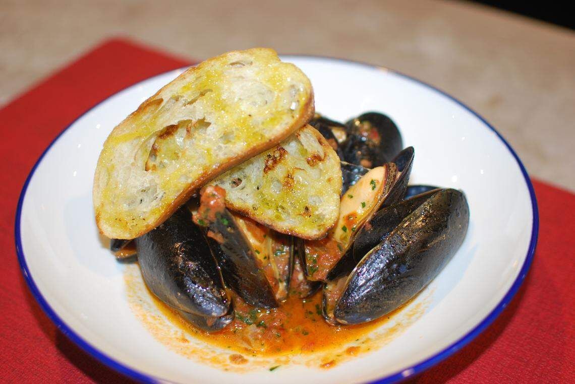 Bowl of mussels in sauce, topped with toasted bread.