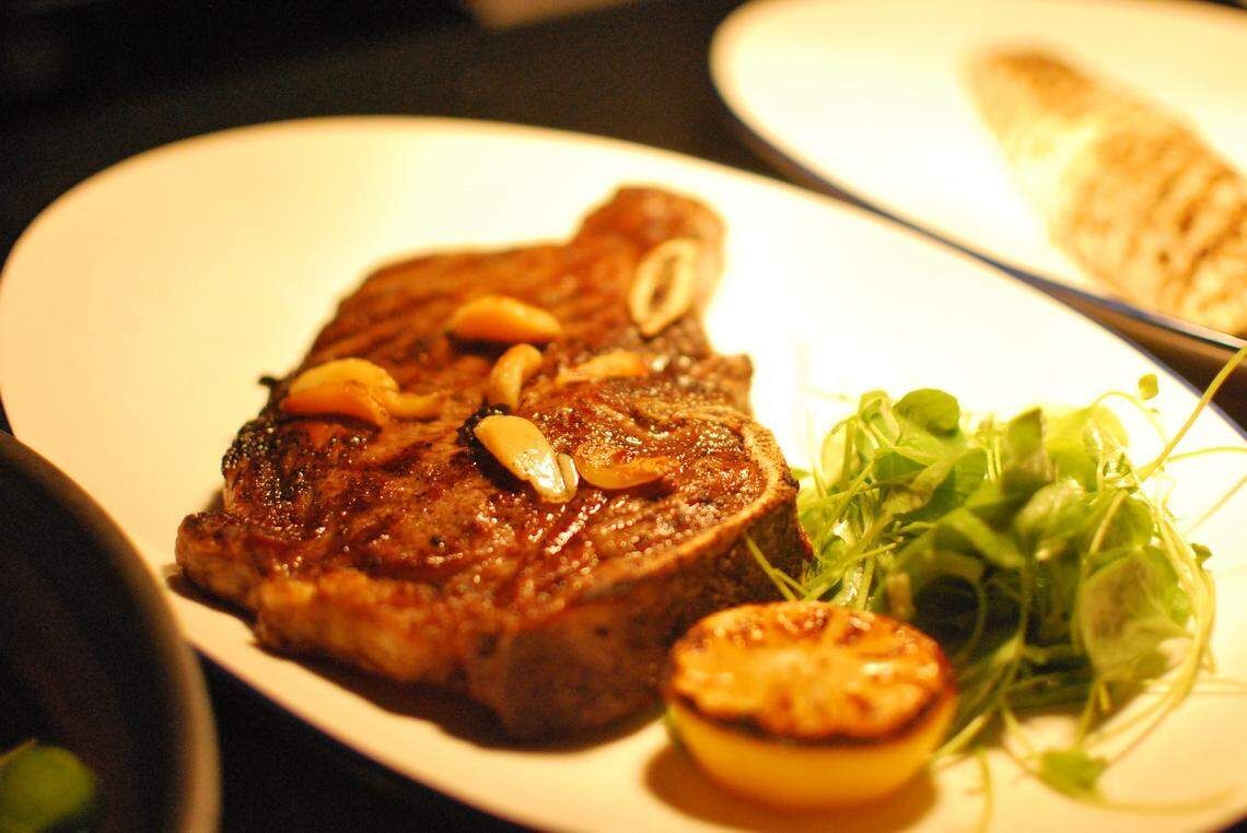 Grilled steak with roasted garlic, lemon, and greens on a white plate.