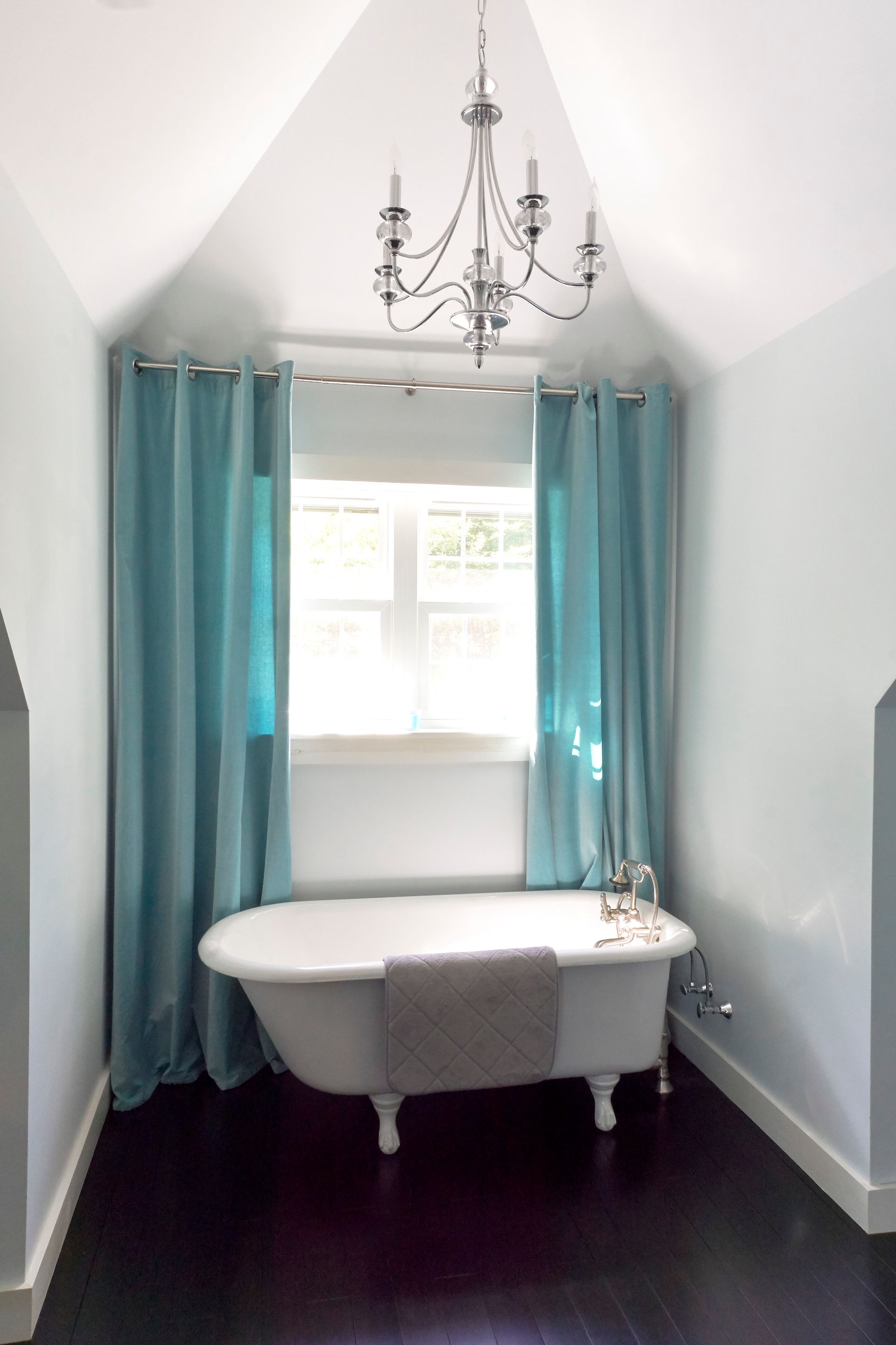 A bathtub in a bathroom with blue curtains and a chandelier