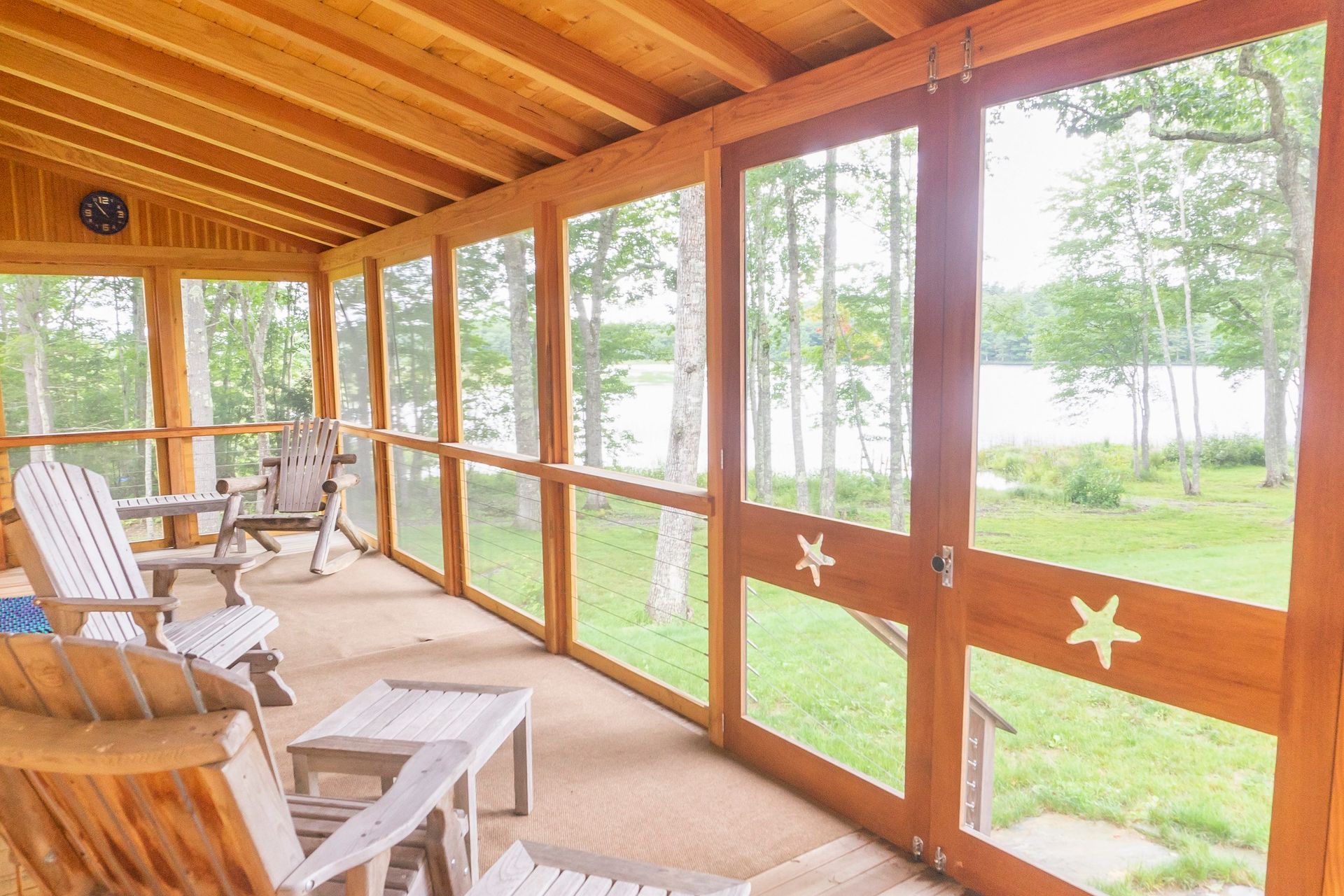 A newly built screened in porch with chairs and a table and a view of a lake near Belfast, Maine.