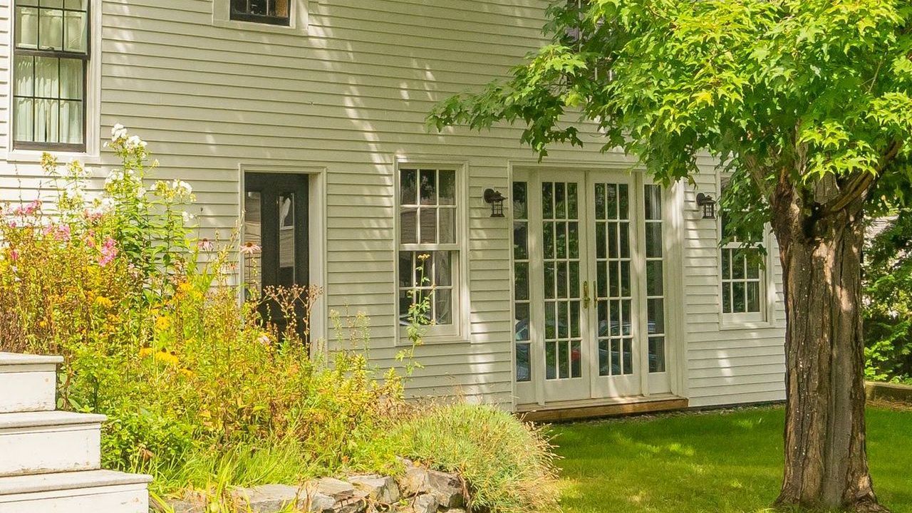 Whitecap Builders' home in Belfast, Maine, with white siding, French doors, a garden, and a large tr