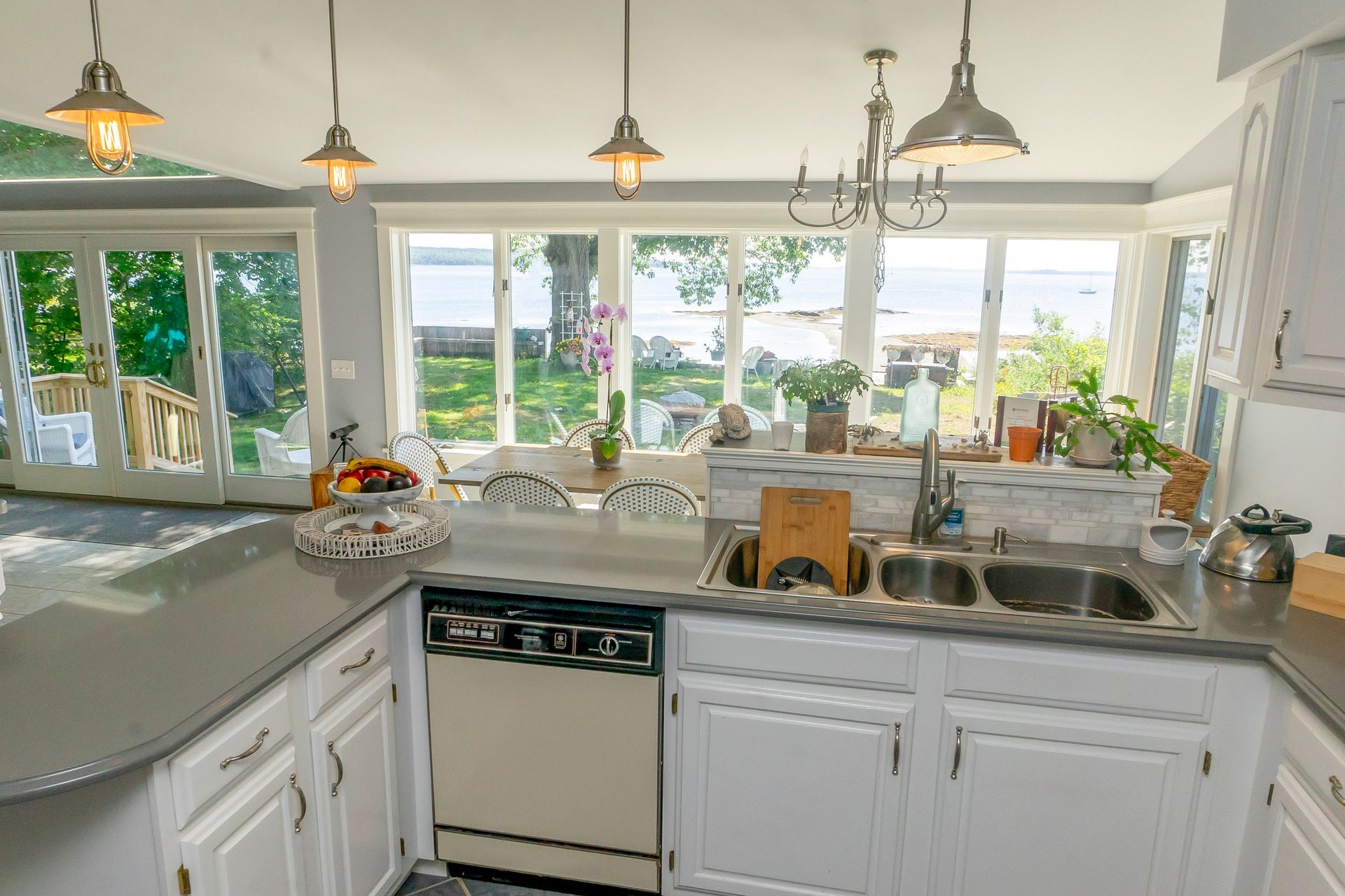 A kitchen with white cabinets , a sink , a dishwasher , and a large window.