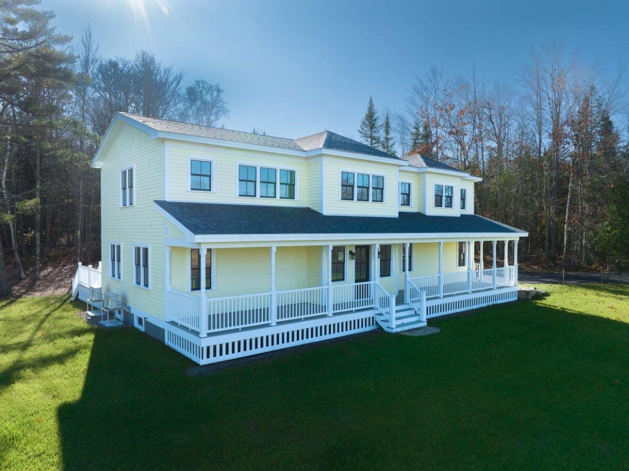 A large yellow custom built house with a large porch is sitting on top of a lush green field.