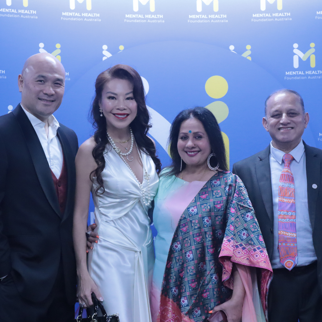Four people posing in front of a blue event backdrop, smiling at the camera.