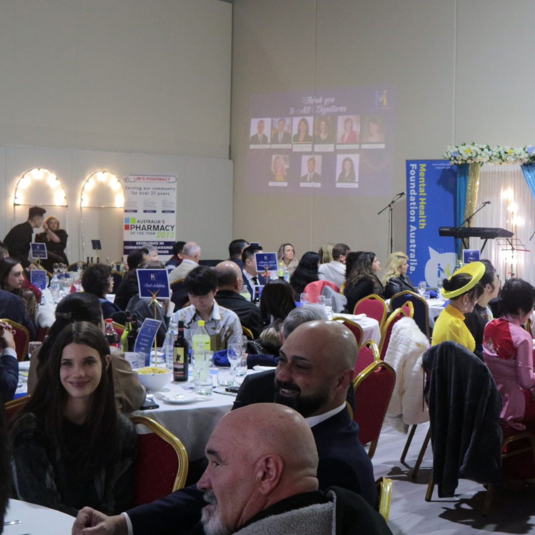 Banquet hall audience seated at round tables, watching a projected presentation on stage
