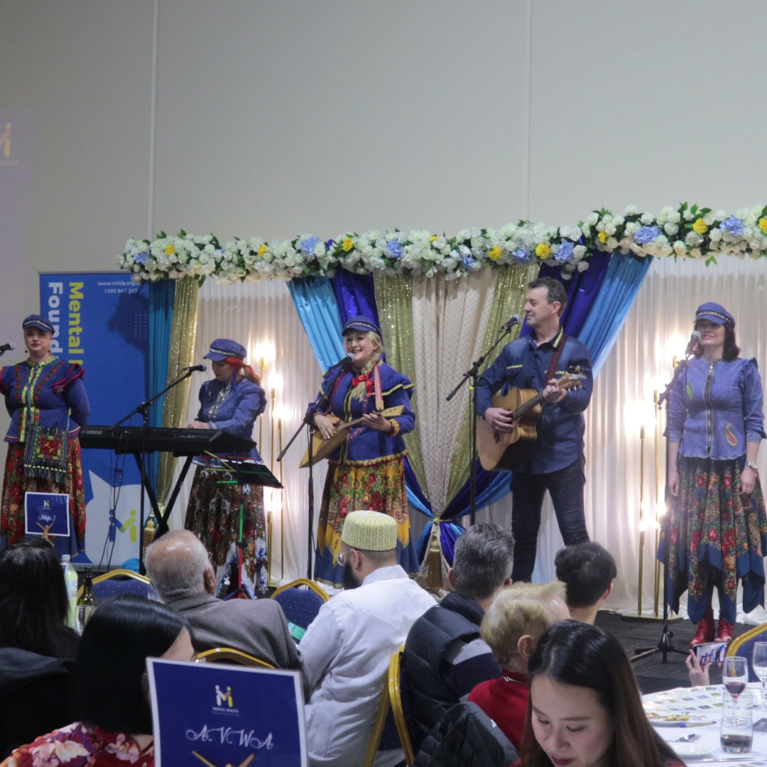 Live band performing onstage at a banquet, with blue drapes, floral arch, and seated audience in the foreground