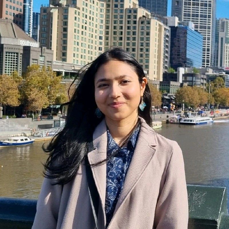 Woman standing by a river with city buildings and boats in the background on a sunny day