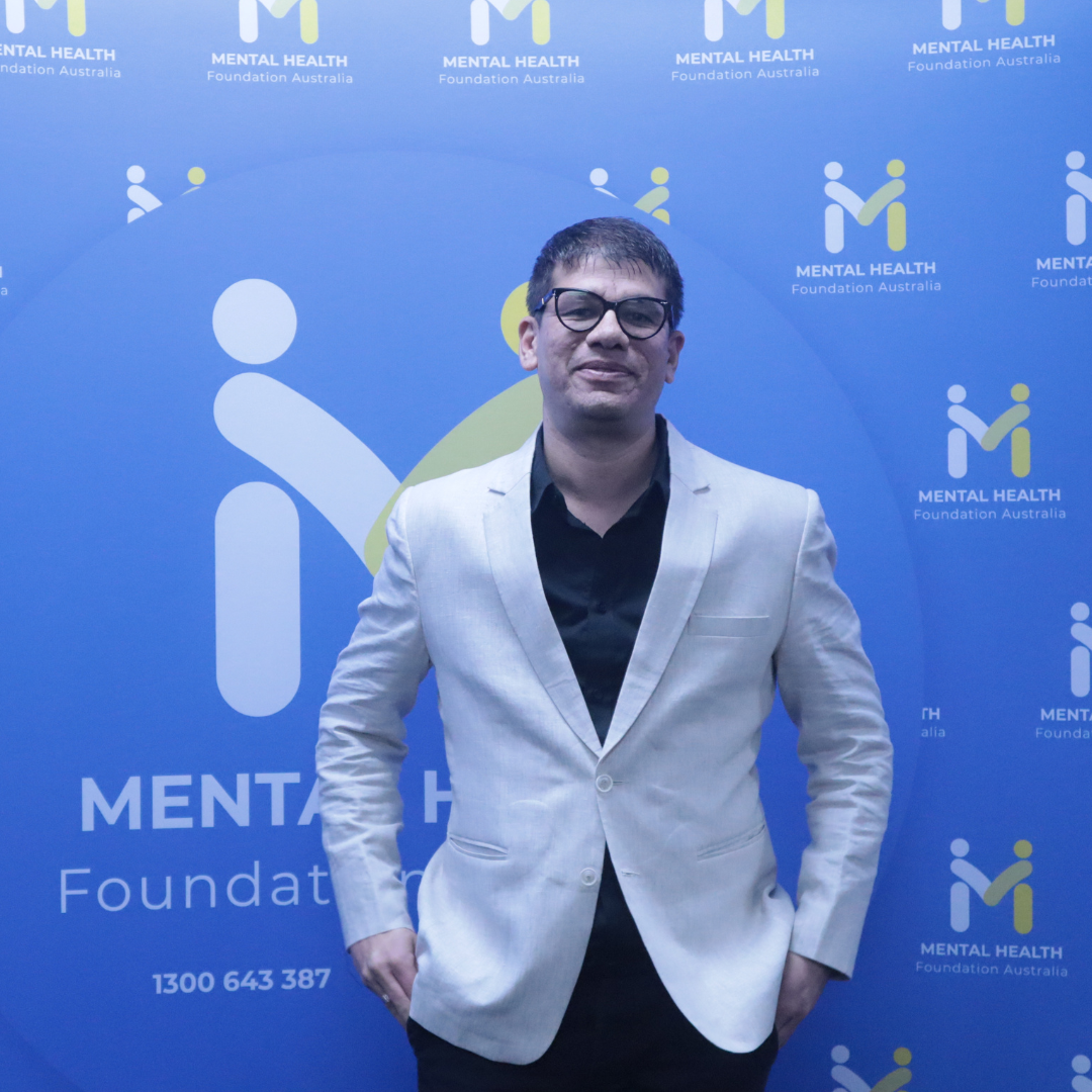 Man in a light blazer standing before a blue Mental Health Foundation backdrop with repeated logos.