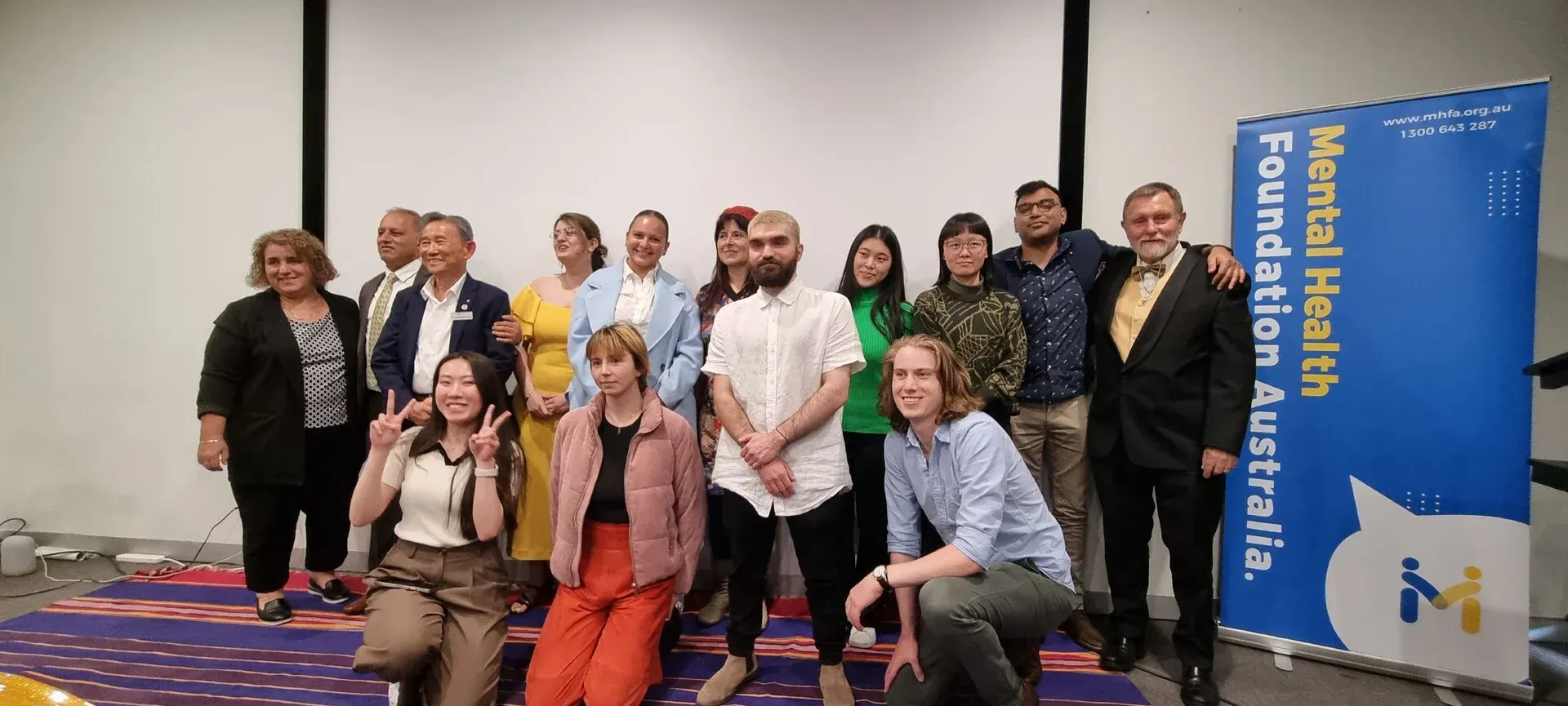 Group of people posing on stage beside a blue conference banner in a meeting room