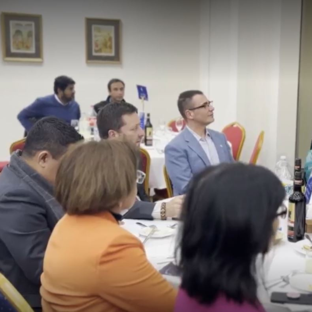 Meeting attendees seated around a conference table in a bright room, listening attentively.