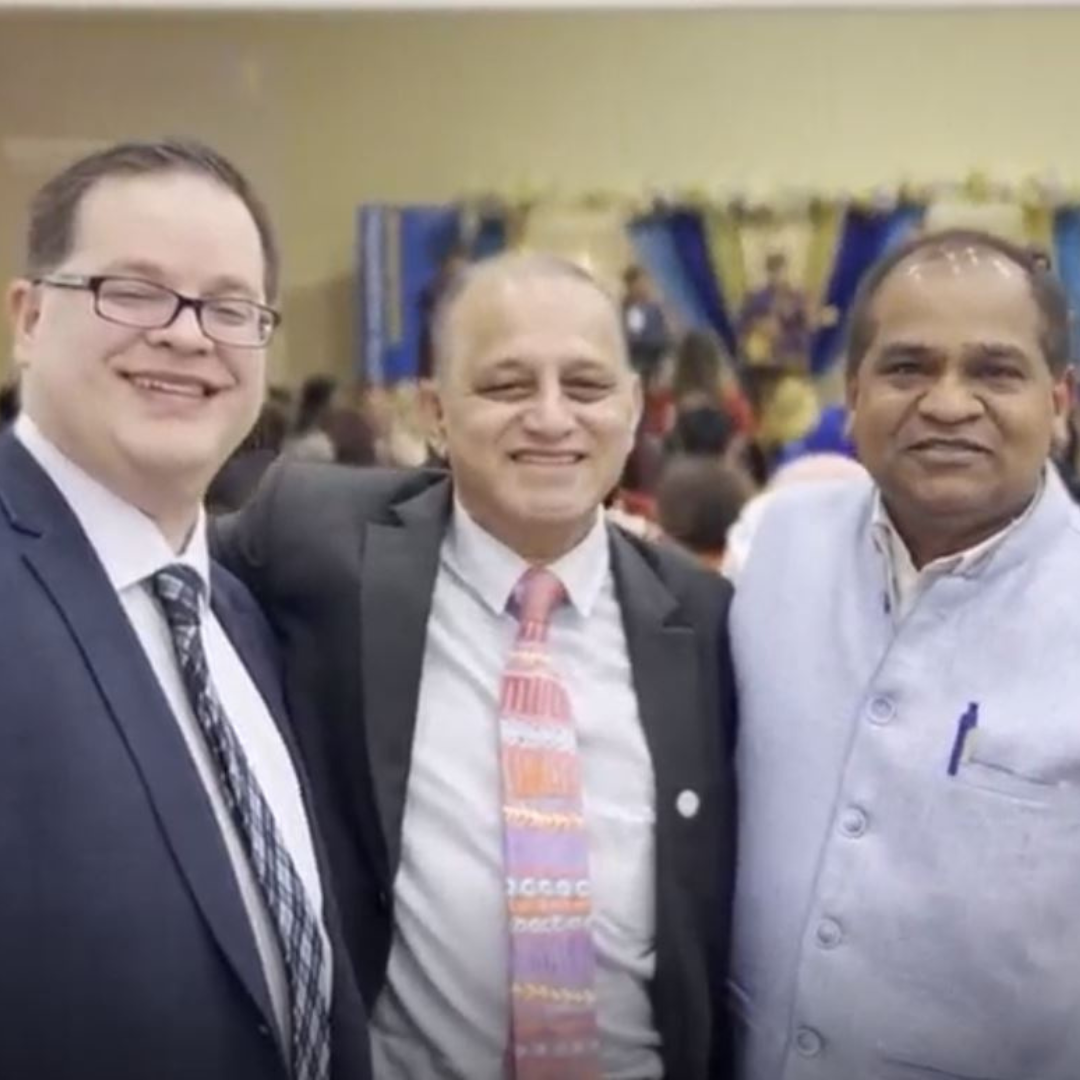 Three men in suits smiling at a formal indoor event.