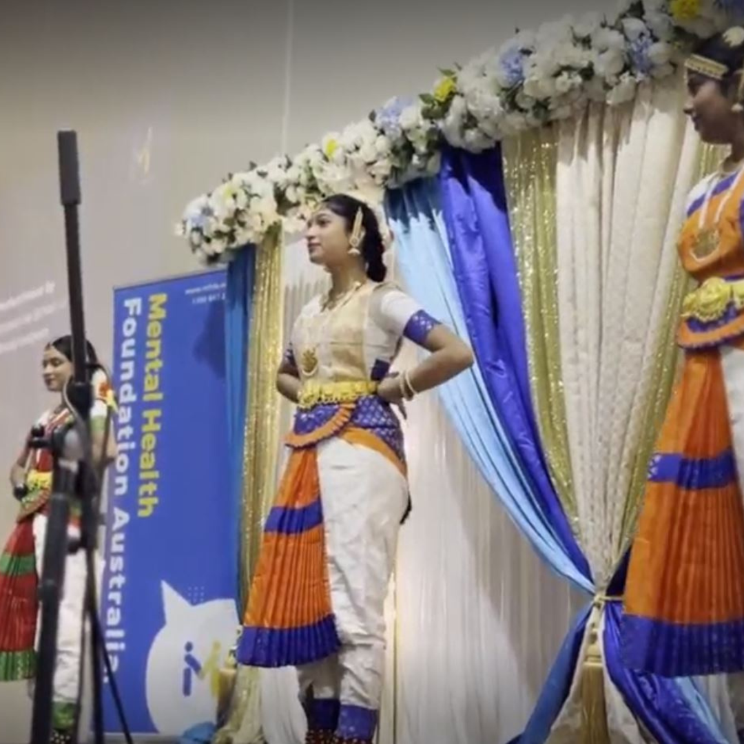 Dancers performing onstage in traditional colorful attire beside a World Health Forum banner