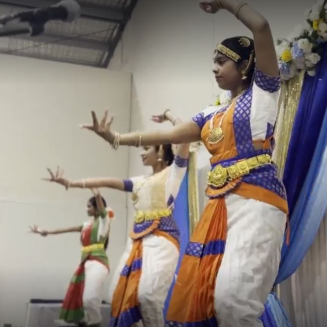 Traditional dancers in colorful costumes performing on a stage with raised arm poses