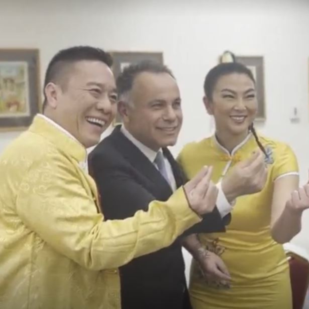 Three people posing indoors, smiling and making finger-heart gestures in yellow and black attire