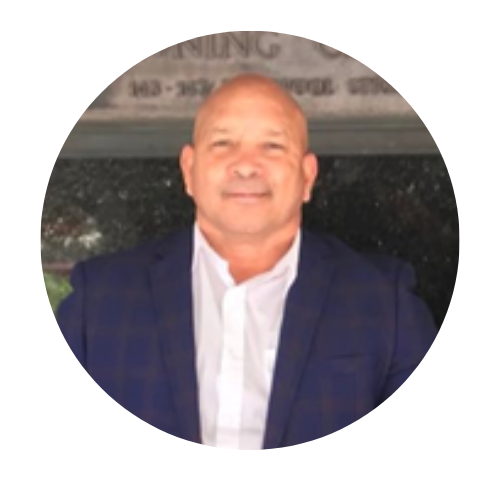Portrait of a smiling bald man in a navy blazer and white shirt against a blurred background