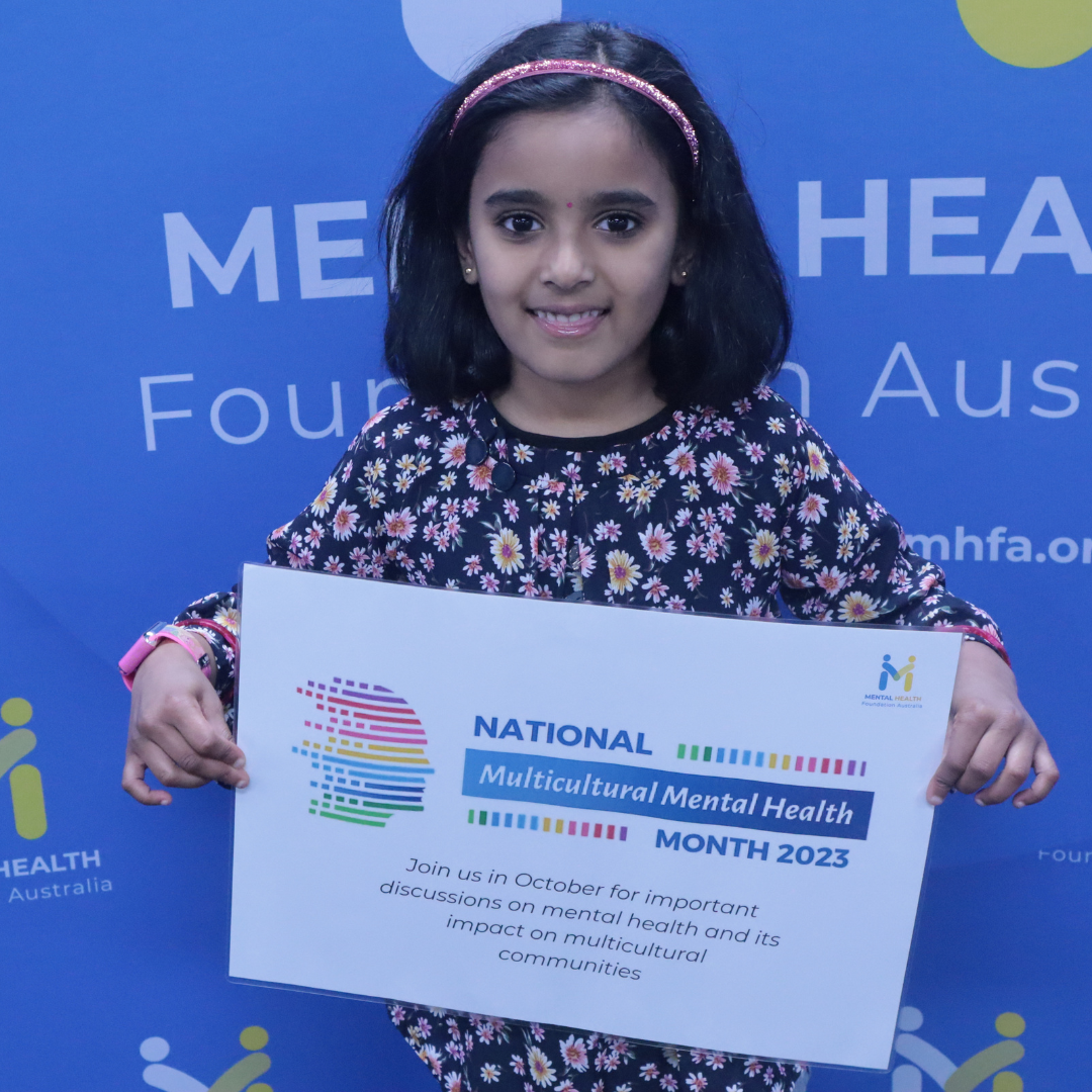 Girl holding a certificate in front of a blue event backdrop for Multicultural Mental Health Month 2023