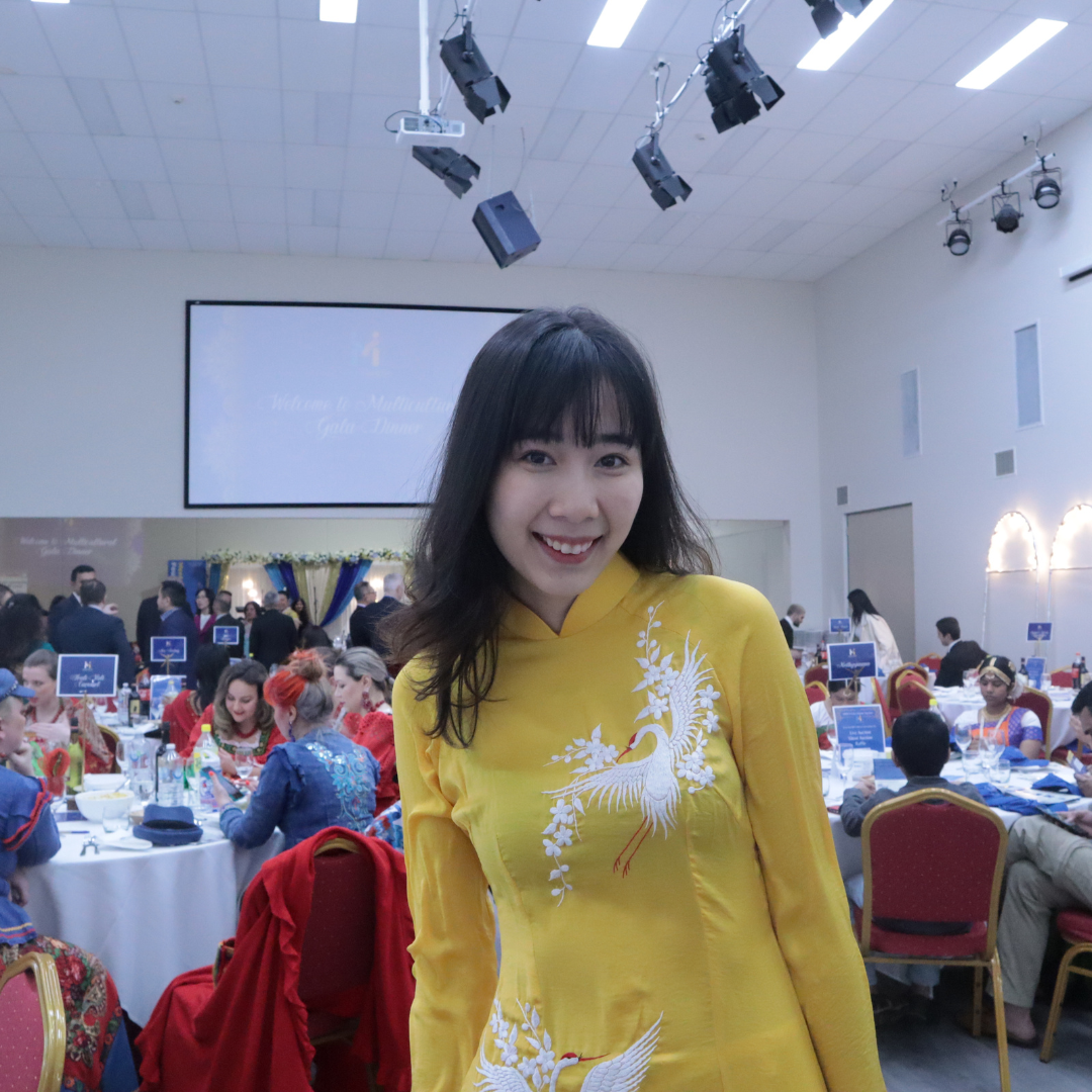 Smiling woman in a yellow dress at a banquet hall with round tables and guests seated in the background