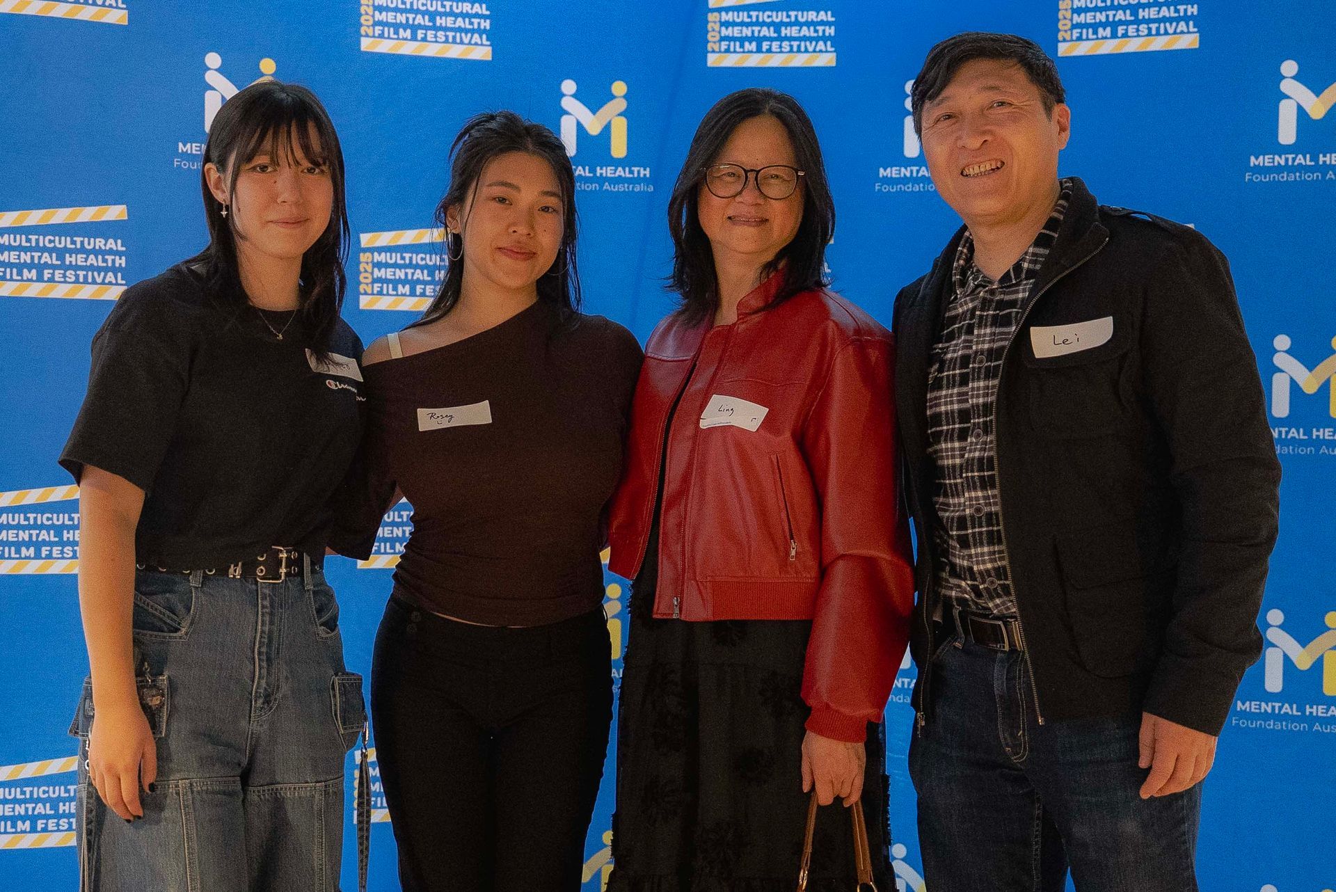 Four people standing together at an event, posing in front of a blue backdrop with white logos.
