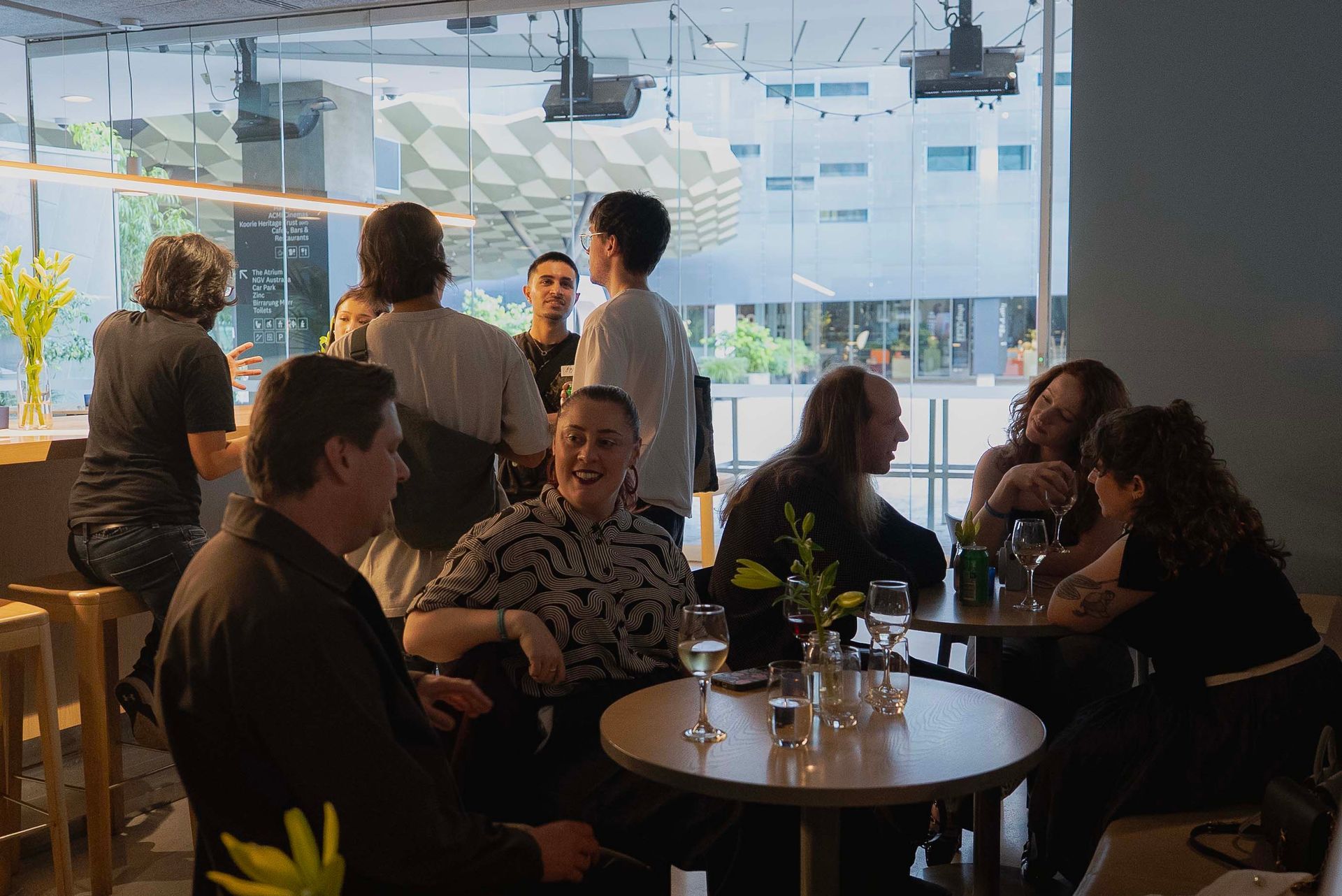 People chatting in a modern cafe with large windows and warm lighting.
