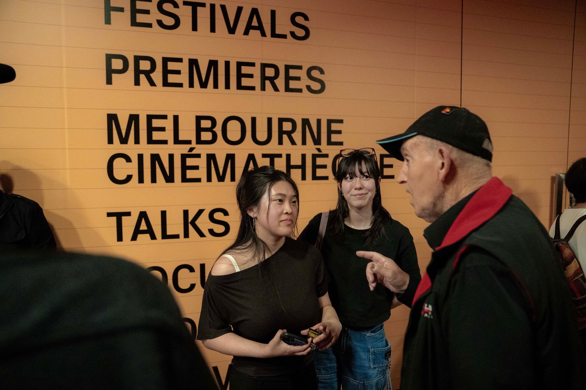 People talking in front of a wall with festival and cinema text at Melbourne Cinémathèque.