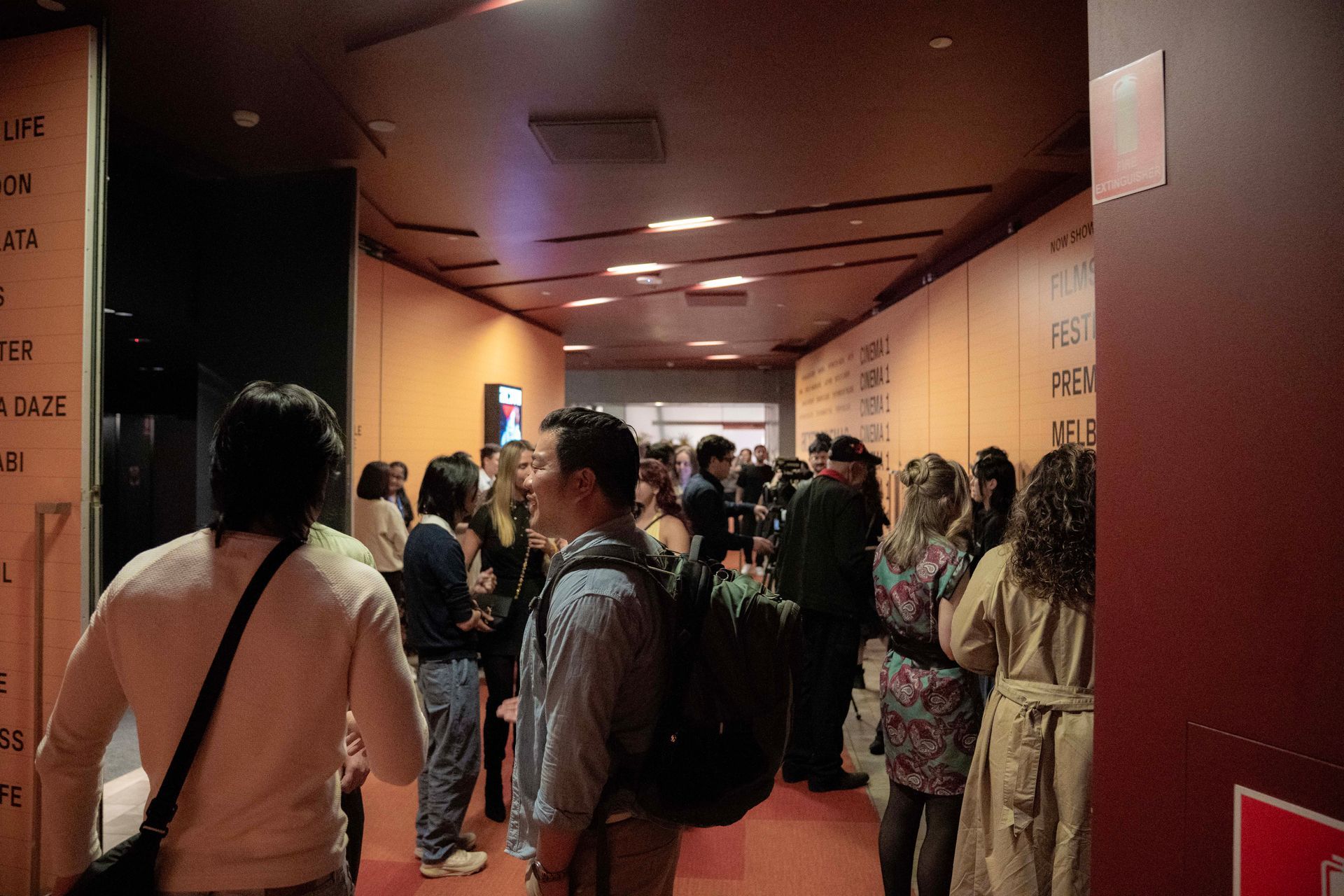 Crowded hallway outside an event room, with people waiting in line under warm ceiling lights.