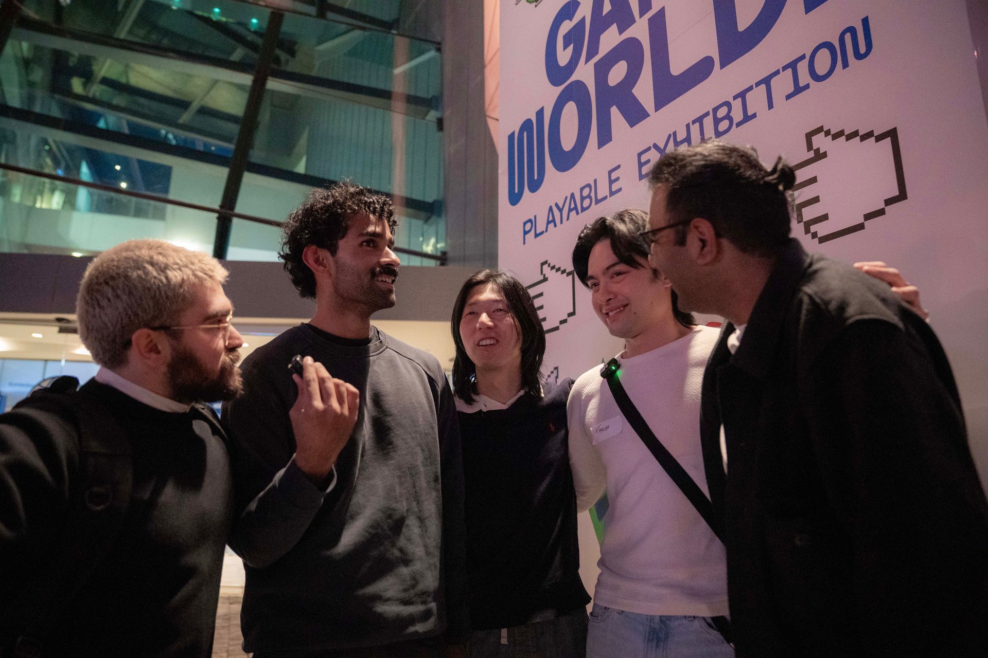 Five people chatting outside a building with a large “WORLD” sign in the background.