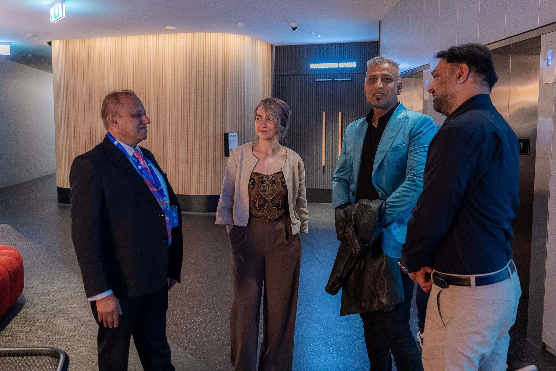 Four people standing and talking in a modern hallway with wood-paneled walls and elevator doors.