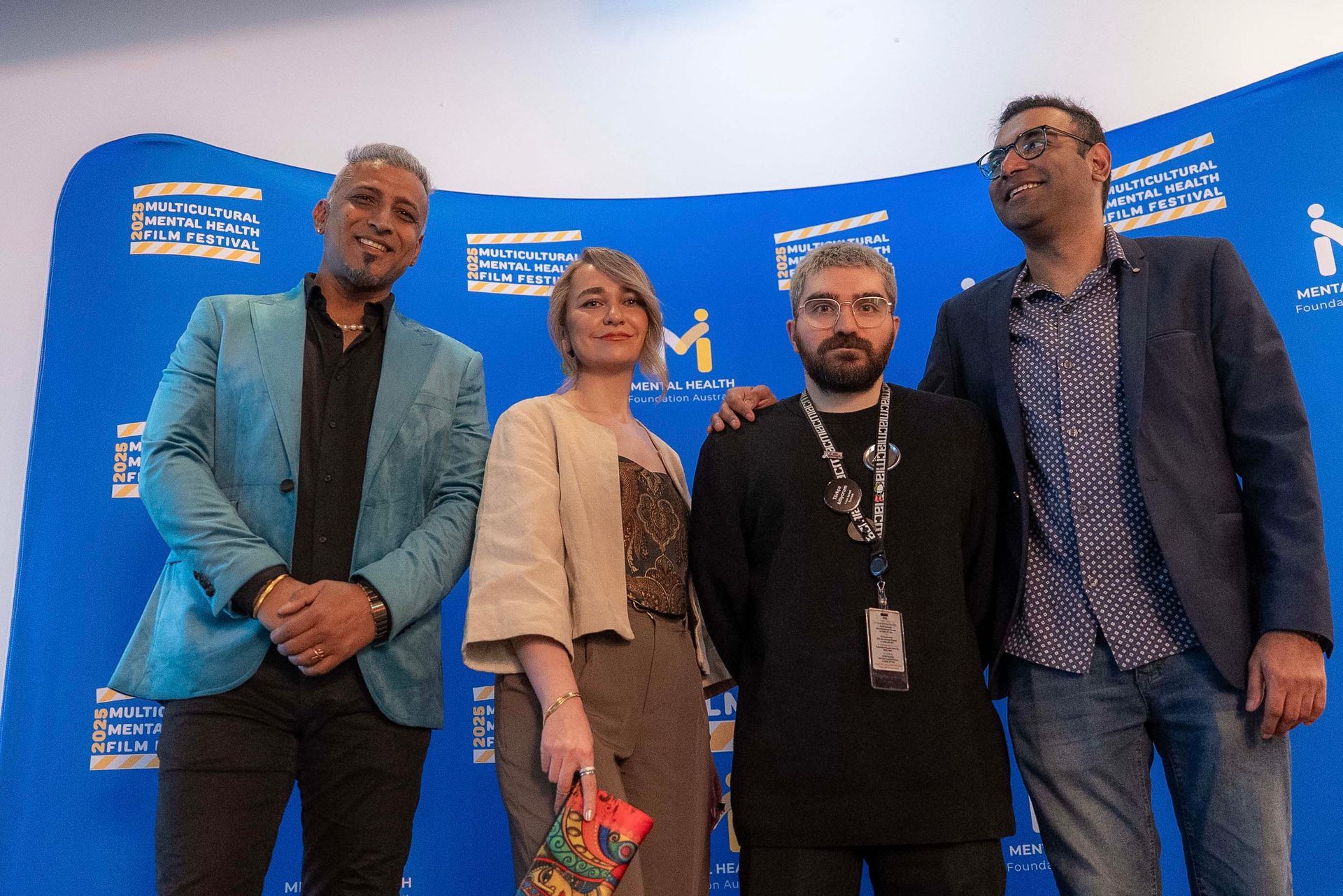 Four people posing on a blue event backdrop, dressed in business and casual attire.