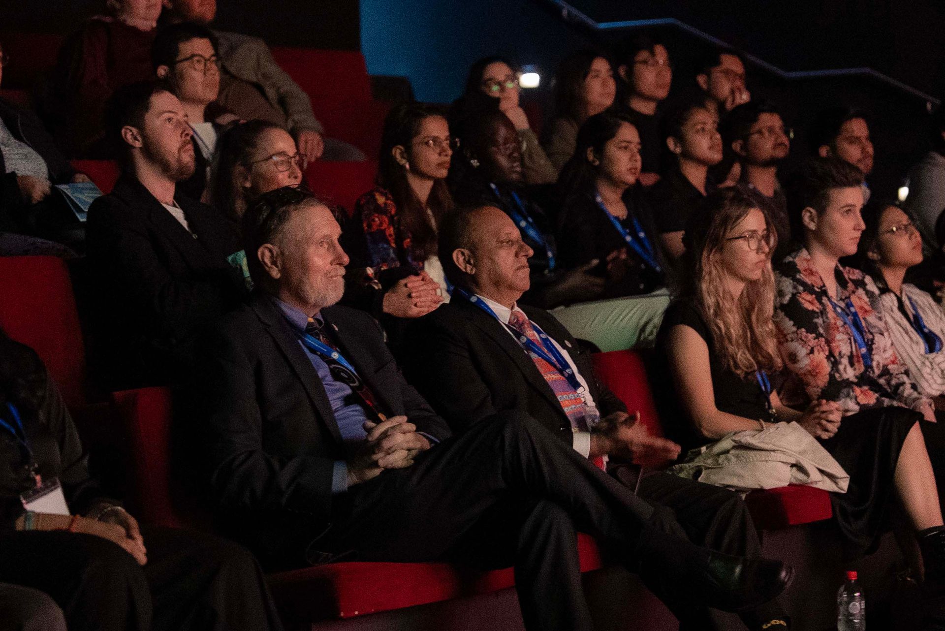 Audience seated in a dark auditorium, watching a presentation on stage