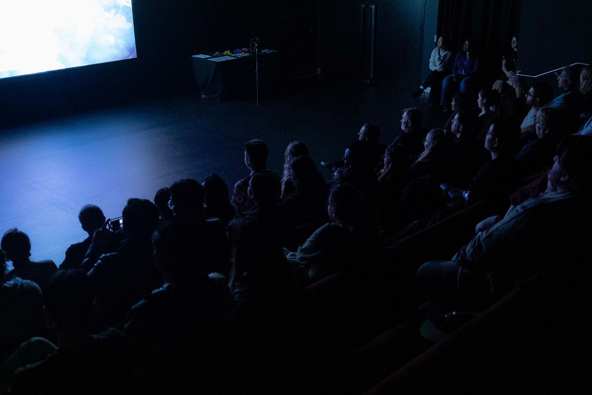 Audience seated in a dark theater watching a blue-lit stage