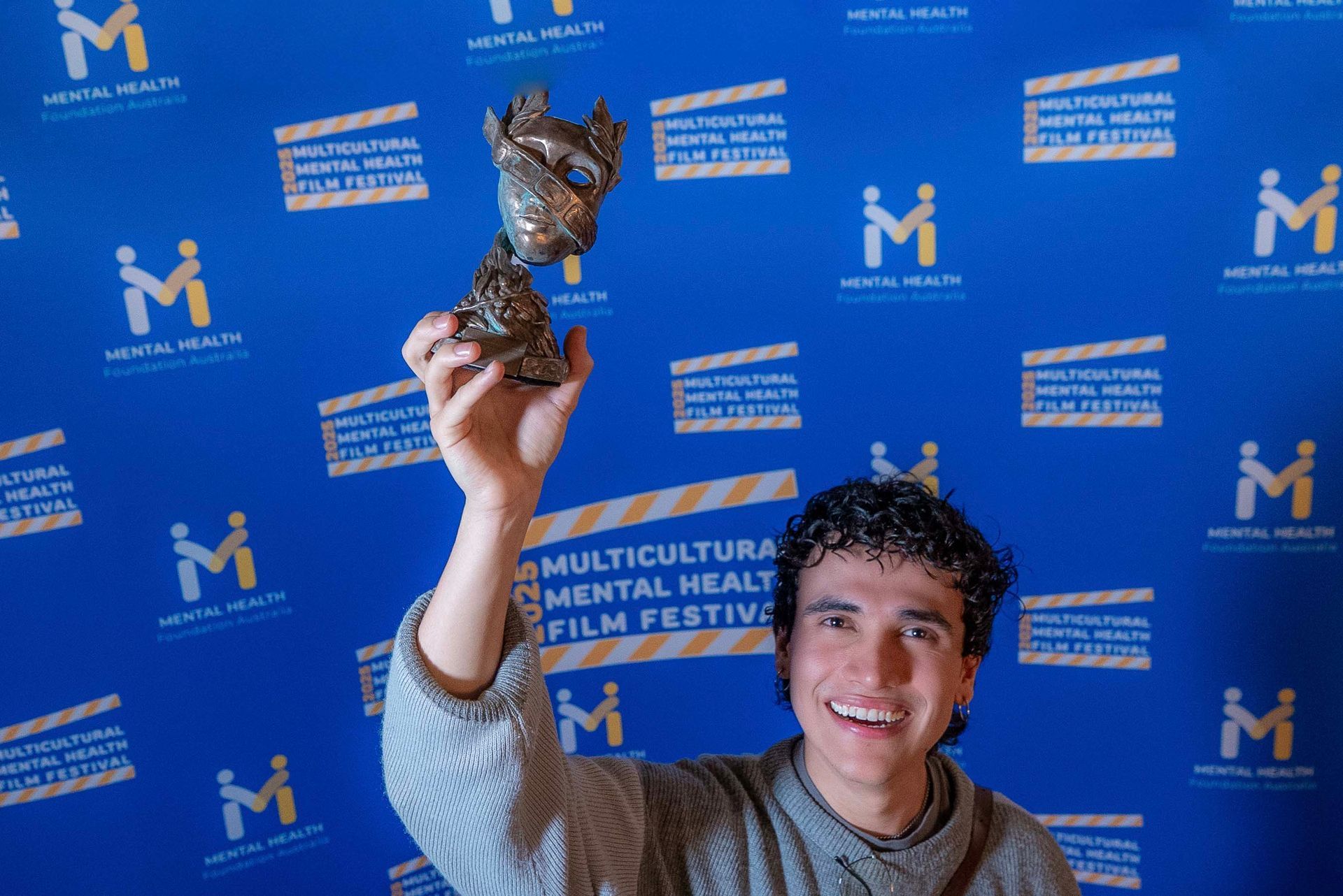 Man holding up a trophy in front of a blue Multicultural Film Festival backdrop