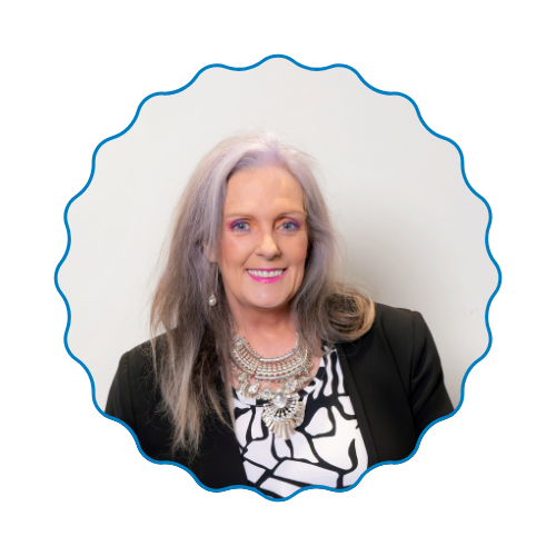 Portrait of a smiling woman with long gray hair in a black blazer and patterned top, framed by a blue scalloped border