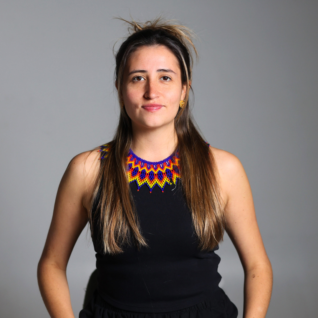 Woman in a black sleeveless top with a colorful beaded neckline, standing against a gray background.