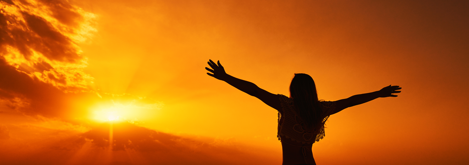 Silhouette of a person with arms outstretched at sunset over an orange sky