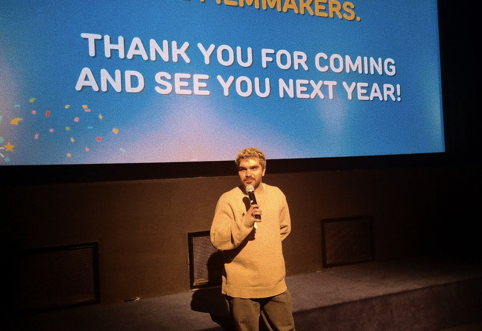 Presenter on stage in front of a blue screen saying, “THANK YOU FOR COMING AND SEE YOU NEXT YEAR!”