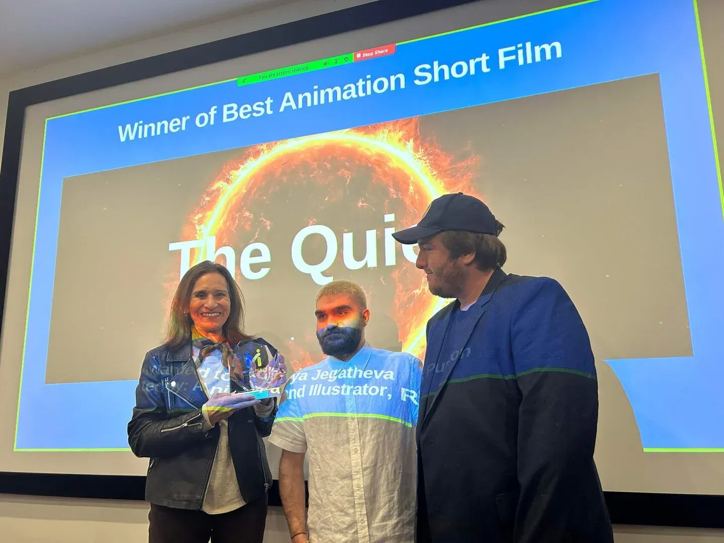 Three people onstage holding an award beneath a screen reading “Winner of Best Animation Short Film”