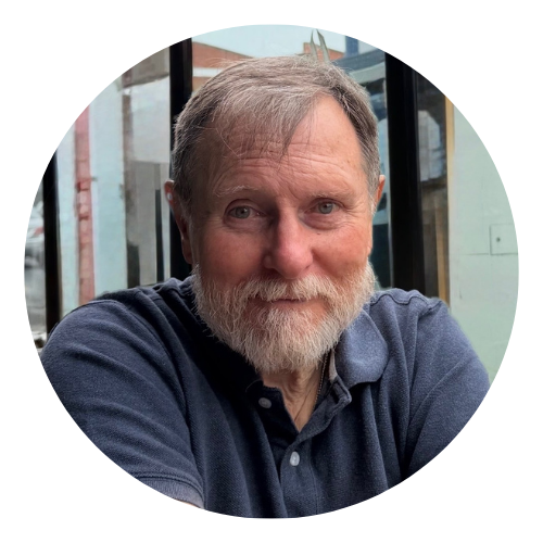 Smiling bearded man in a navy shirt seated by a window