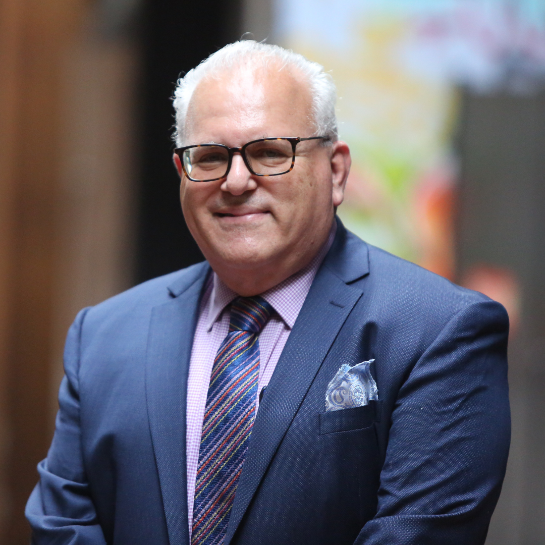 Portrait of a smiling man in a blue suit and striped tie, standing indoors
