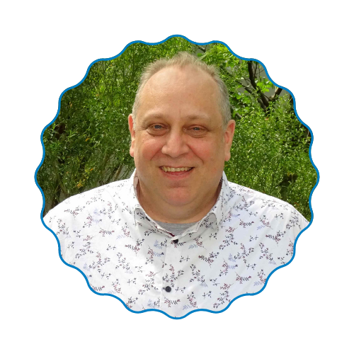 Smiling person in a white patterned shirt, framed by a blue scalloped border against green foliage.