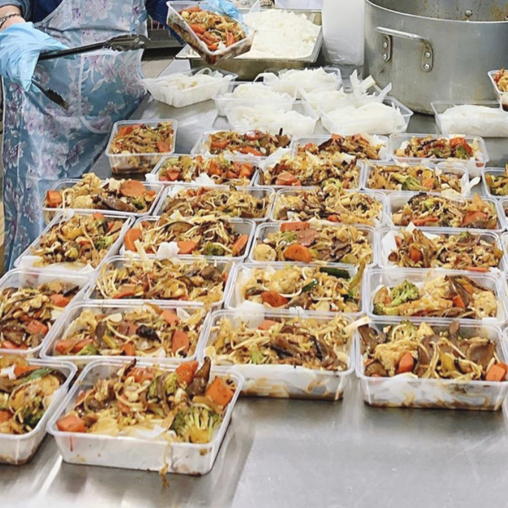 Rows of takeout containers filled with stir-fry being packed on a kitchen table