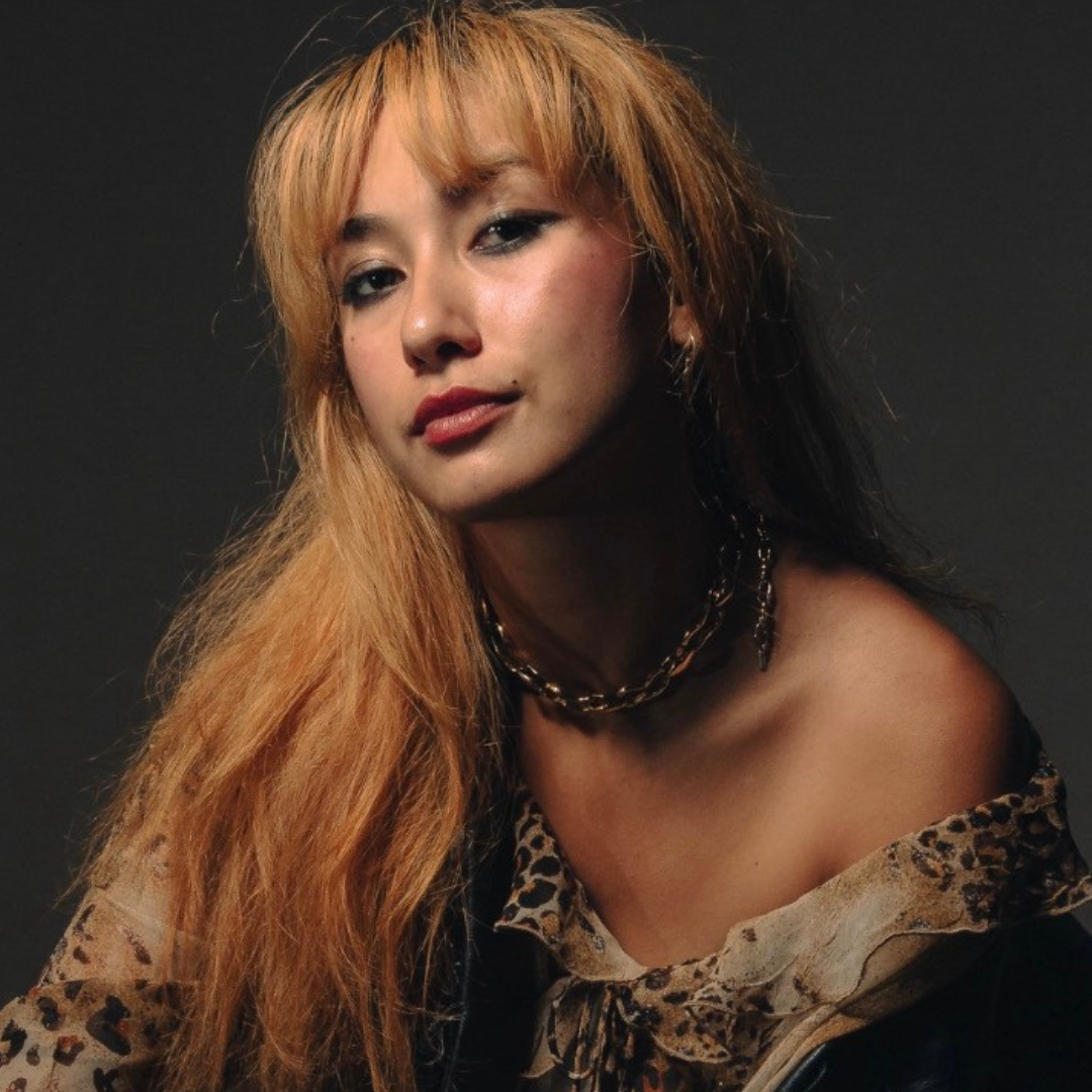 Portrait of a woman with long blonde hair in an off-shoulder leopard-print top against a dark background