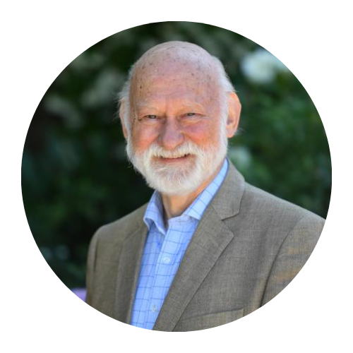 Portrait of a smiling bearded man in a light gray blazer and blue shirt against a blurred green background