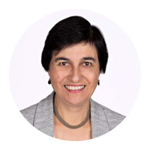 Headshot of a smiling person with short dark hair, wearing a gray blazer and necklace on a white background